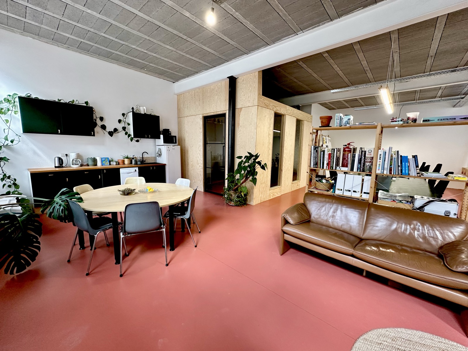 The common room looking towards the kitchen, with a leather sofa, bookshelves and the plywood meeting box.