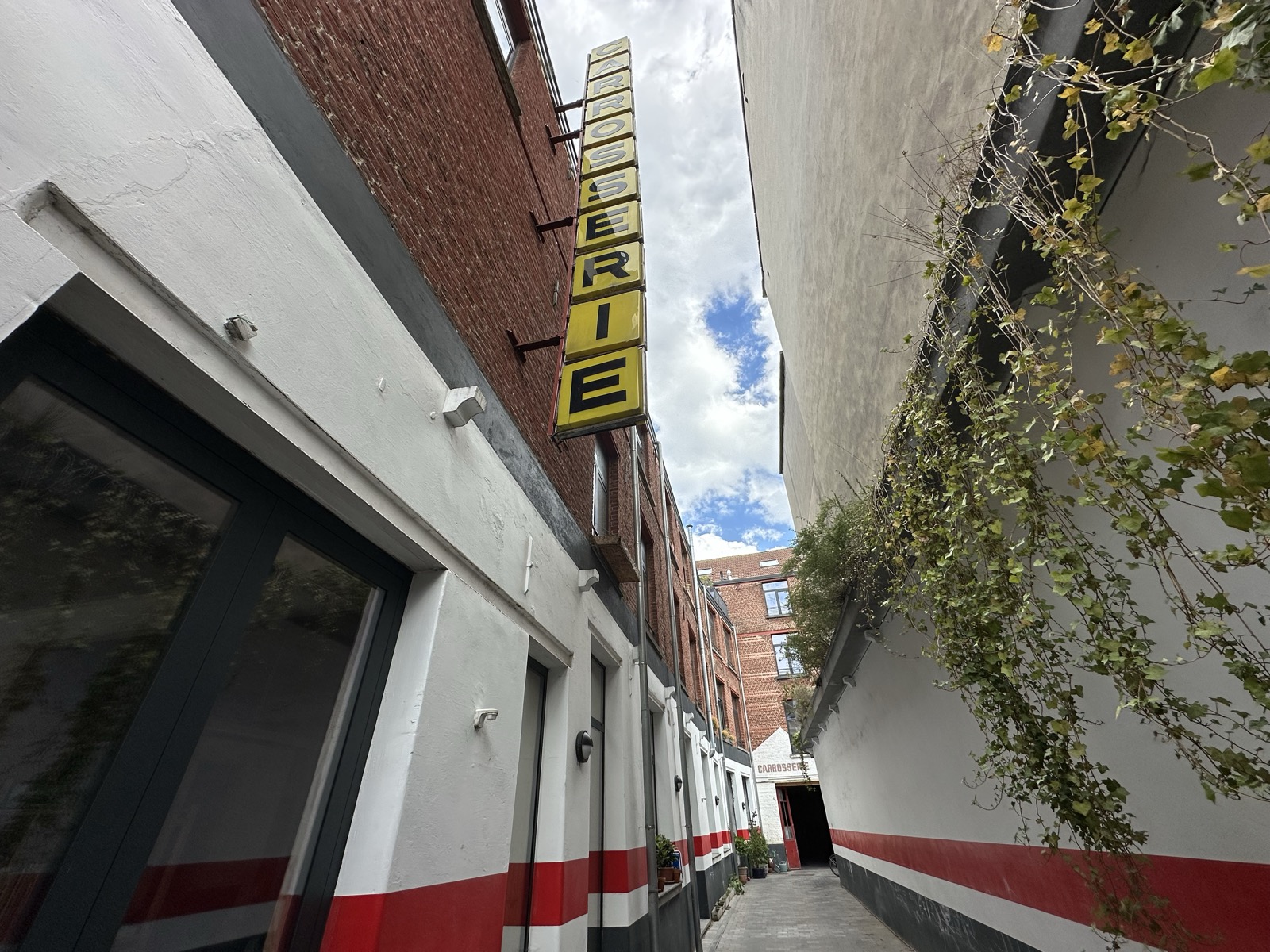 The alley beside the building, with the old yellow CARROSSERIE sign still mounted on the brick wall.