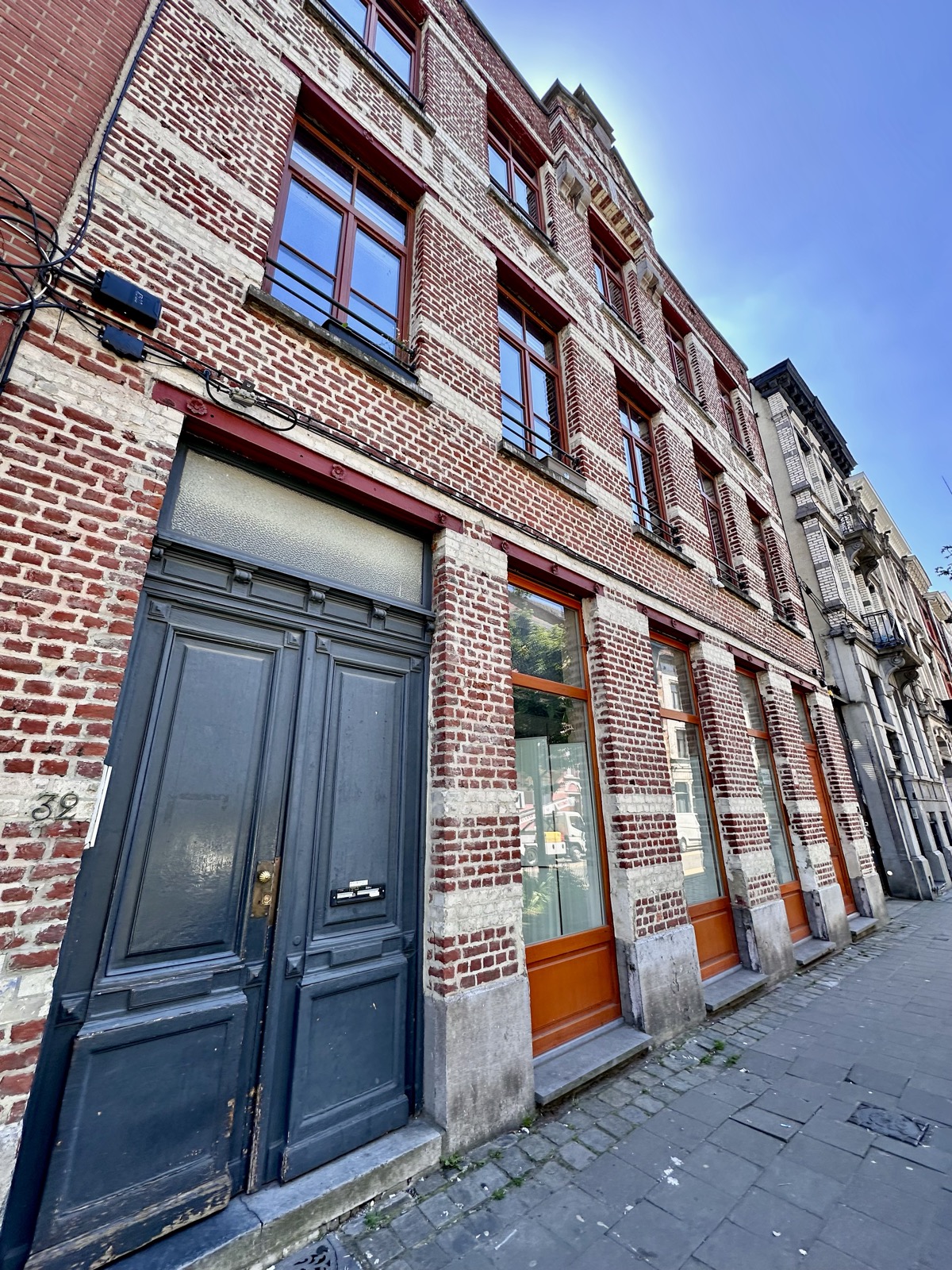 The street facade on Rue Georges Moreau: red and white brick, tall orange-framed windows and a dark double door at number 32.